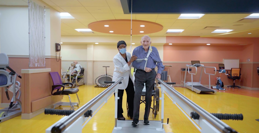 A healthcare professional assists an elderly patient during a physical therapy session, focusing on walking and rehabilitation.