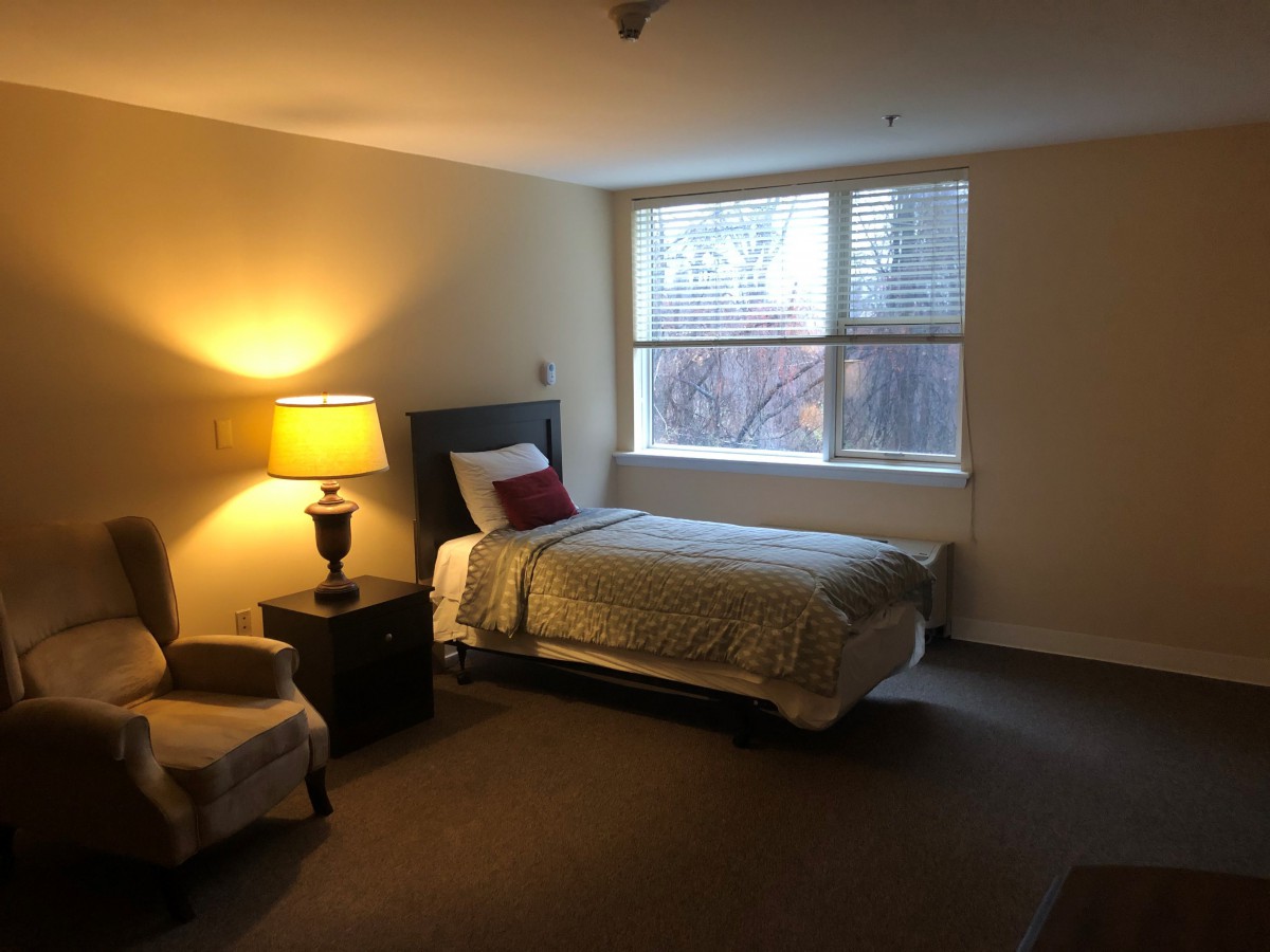 A cozy bedroom with a single bed and a warm lamp by the window.