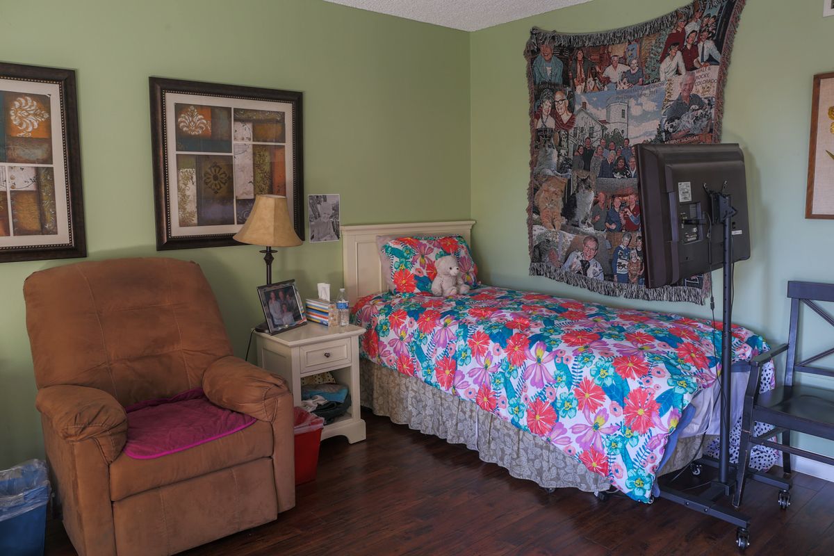A cozy bedroom featuring a single bed with a colorful quilt, an armchair, and various wall decorations.