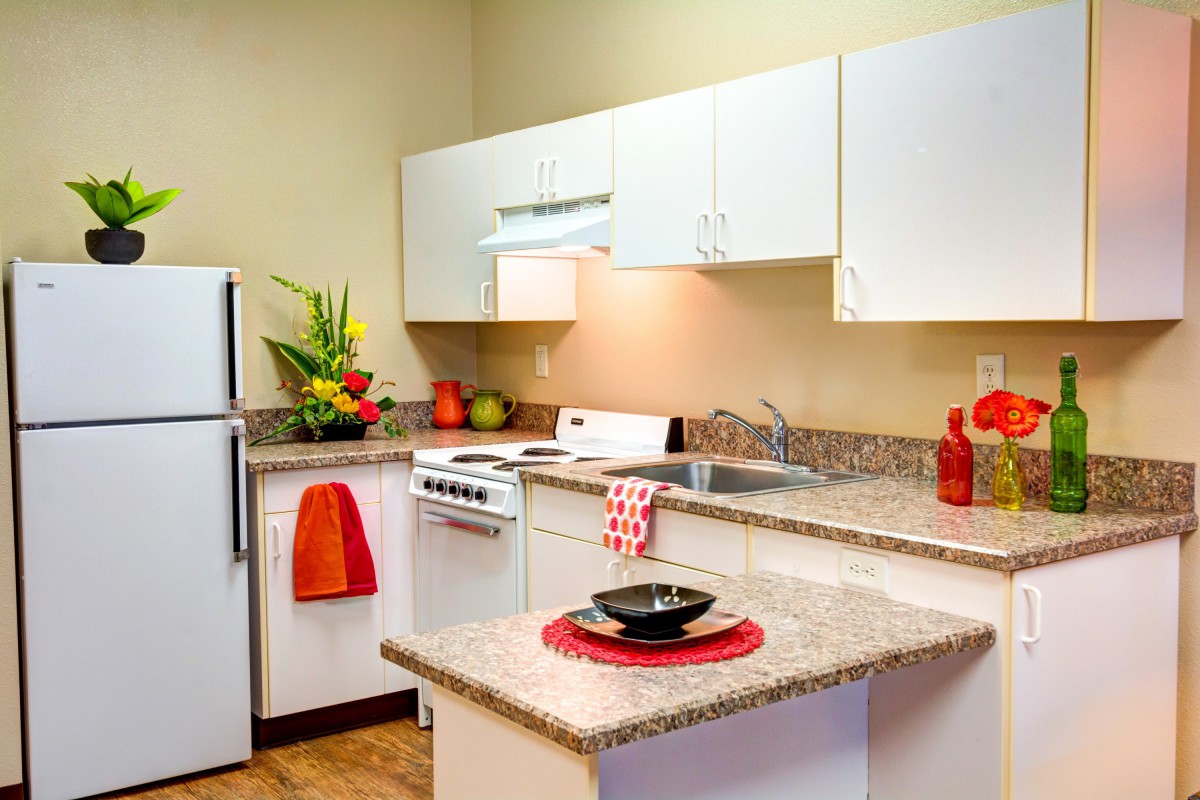 A modern kitchen with white cabinets and red accents, featuring a sink, stove, and refrigerator.