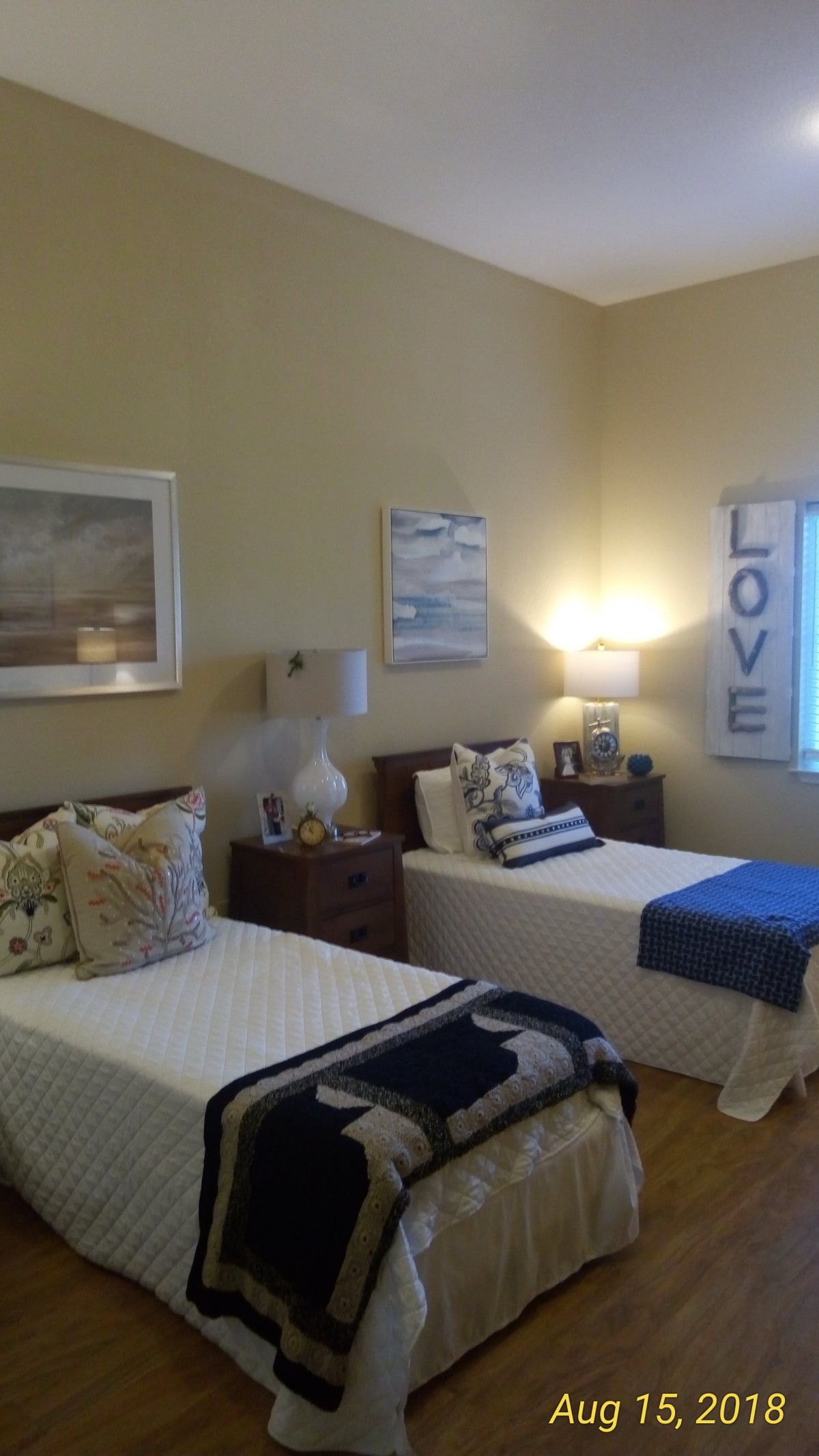 A cozy bedroom featuring twin beds with decorative pillows, warm lighting, and wall art.