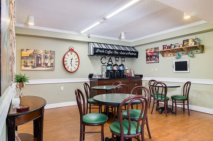 A cozy cafe interior featuring round tables, chairs with green cushions, a coffee station, and vintage decor.