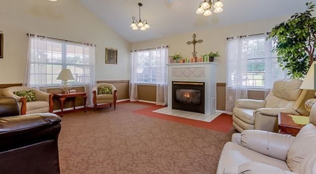A cozy living room featuring a fireplace, armchairs, and elegant lighting with natural light streaming through the windows.