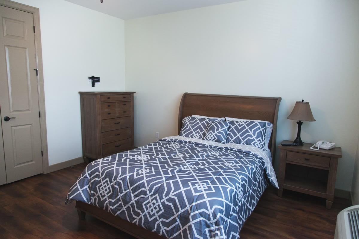 A neatly arranged bedroom with a wooden bed, dresser, and a side table lamp.