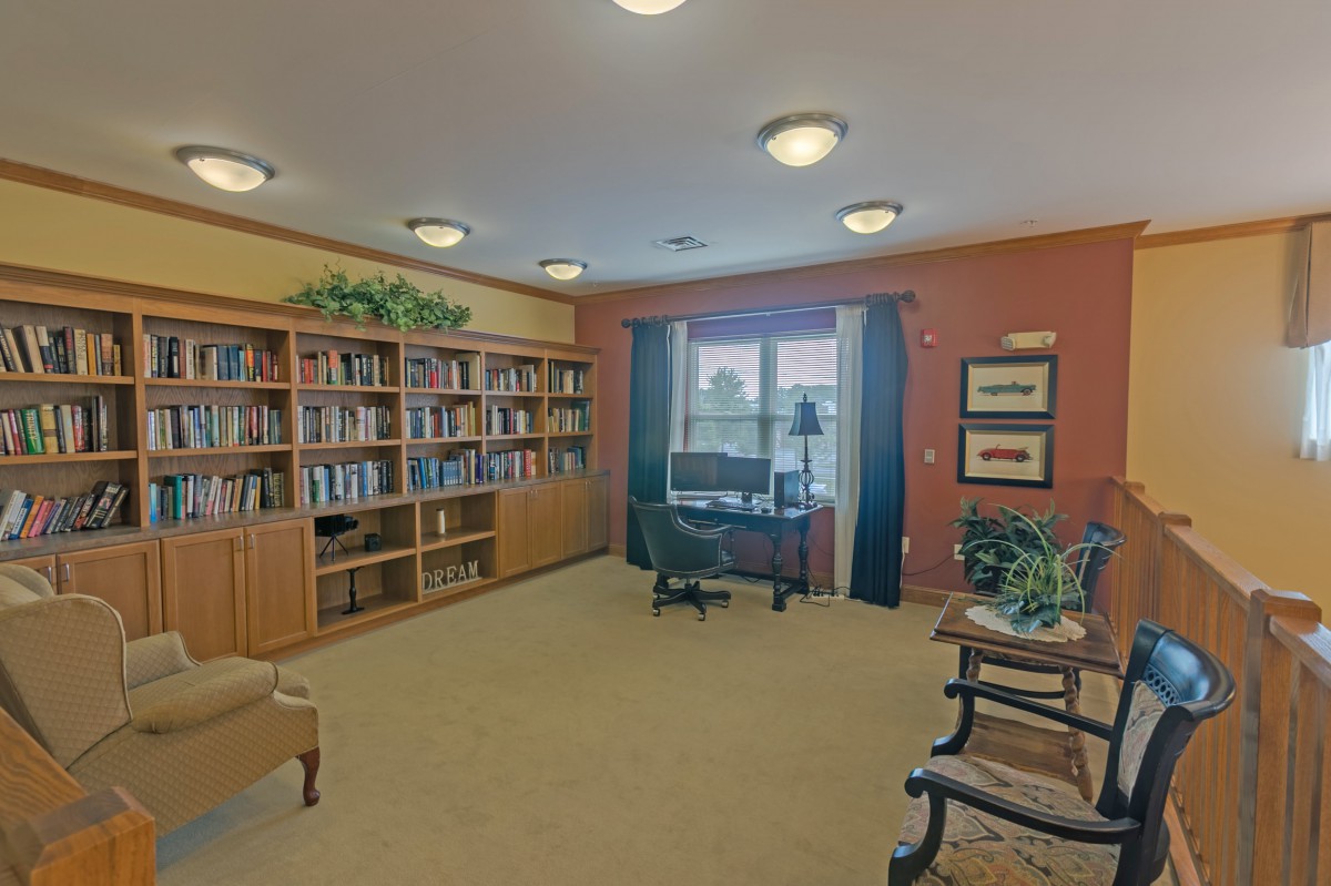 A cozy library with bookshelves, a desk, and seating area by a window.