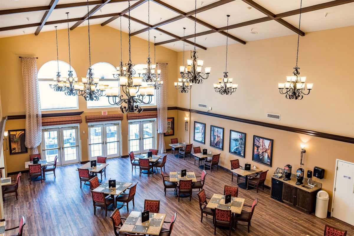 A spacious dining area with elegant chandeliers, wooden flooring, and neatly arranged tables and chairs.