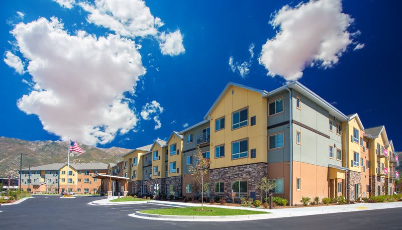 A modern residential apartment complex under a bright blue sky with fluffy clouds.