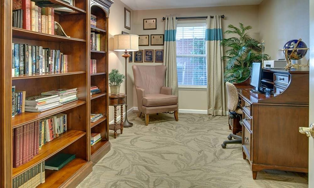 A cozy home office with bookshelves, an armchair, and a desk by the window.