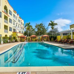A serene outdoor swimming pool area at a hotel surrounded by palm trees and clear blue skies.