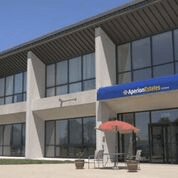A modern office building with large glass windows and an outdoor seating area under a blue awning.