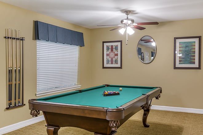 A cozy game room with a pool table, adorned with framed artwork and a ceiling fan.