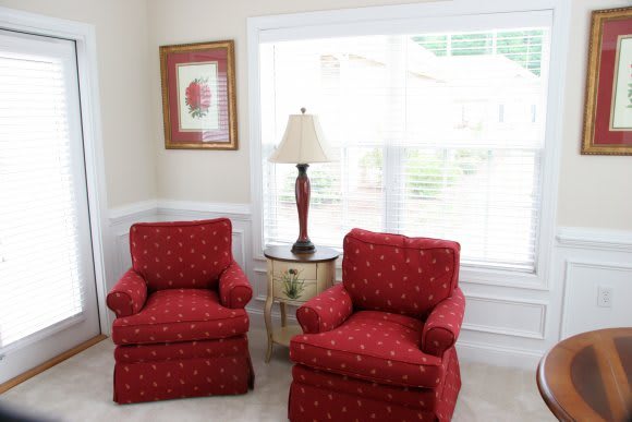 A cozy living room corner with two red armchairs, a lamp, and a side table by the window.