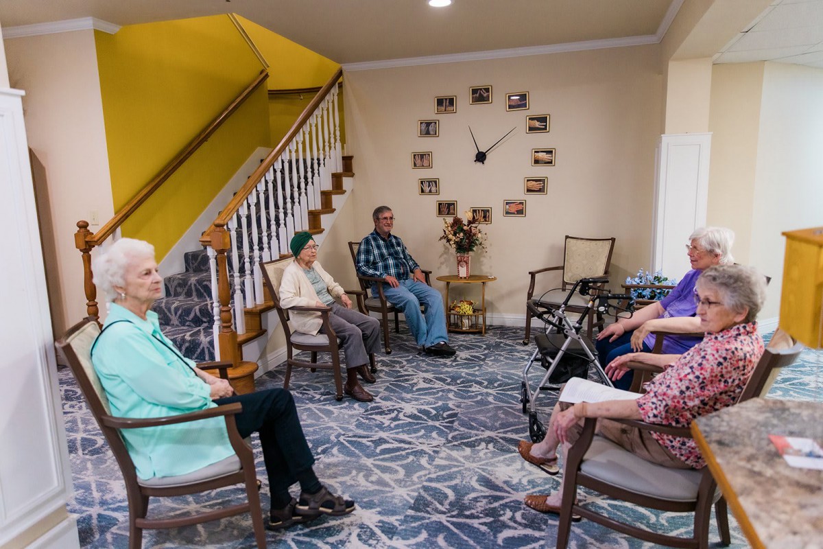 A group of seniors seated in a living room, engaged in a casual meeting.