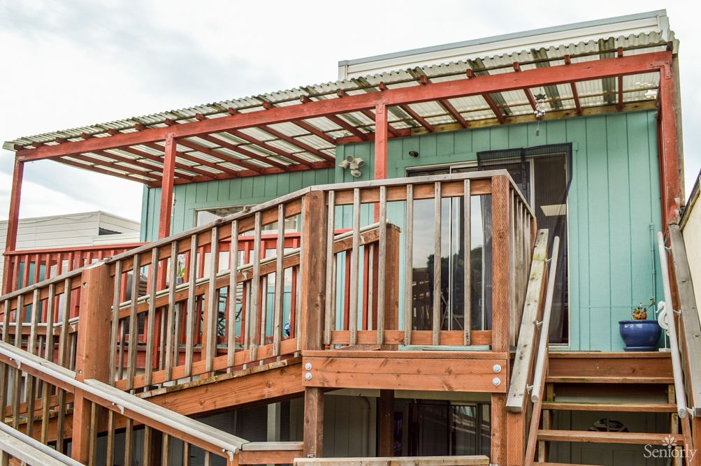 A wooden deck with stairs leading to a house, featuring a pergola above.