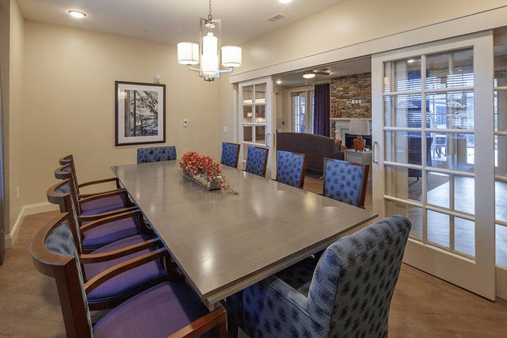A stylish dining room with a large conference table surrounded by patterned chairs, featuring elegant lighting and wall artwork.
