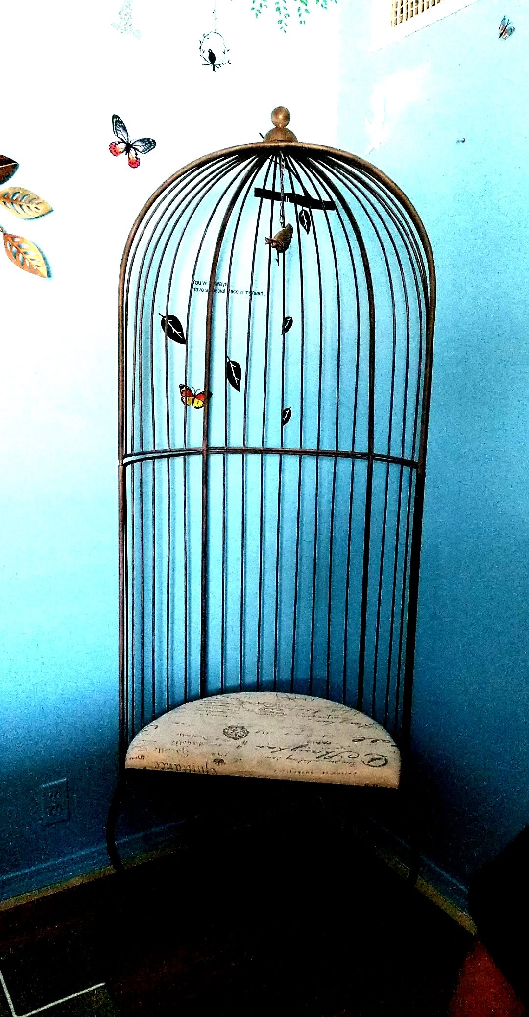 A decorative birdcage with a butterfly and leaves set against a blue background.