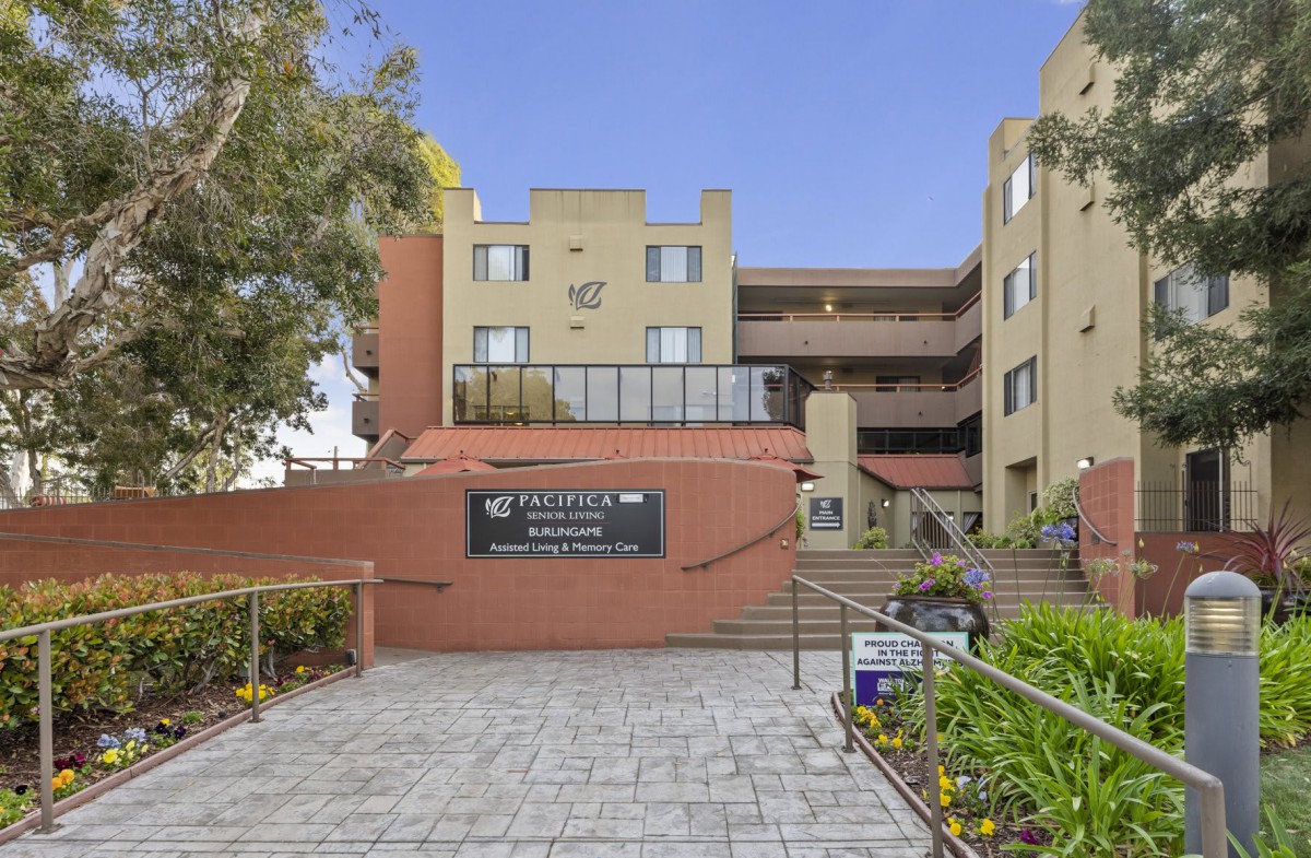 The entrance of an apartment complex featuring modern architecture and well-maintained landscaping.