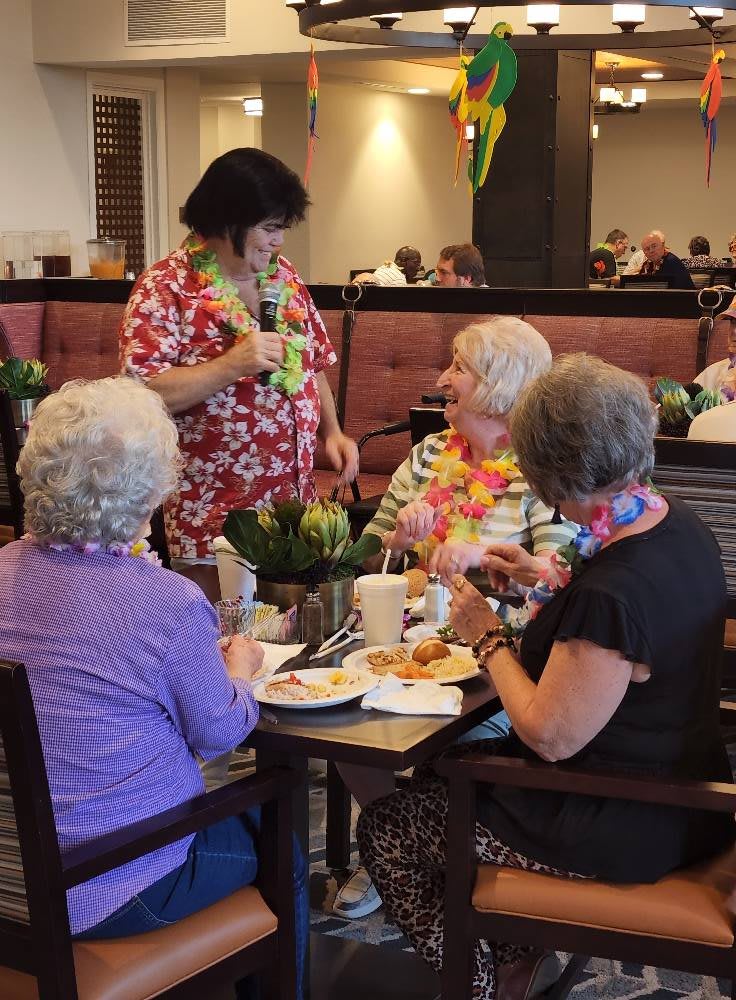 A group of seniors enjoying a meal together, adorned with leis, engaging in lively conversation.