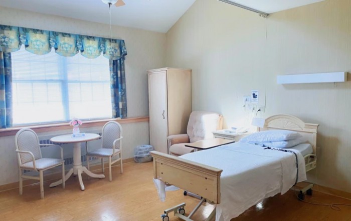 A clean and well-lit hospital room with a bed, table, and chairs.