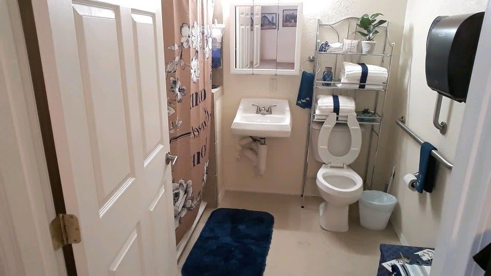 A tidy bathroom with a sink, toilet, and shower area, featuring neatly arranged towels and a blue bath mat.