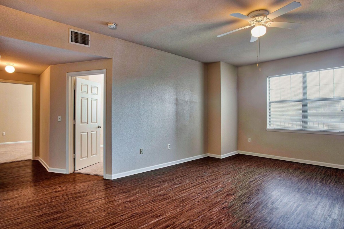 An empty room with wood flooring and a ceiling fan, featuring a window and a doorway.