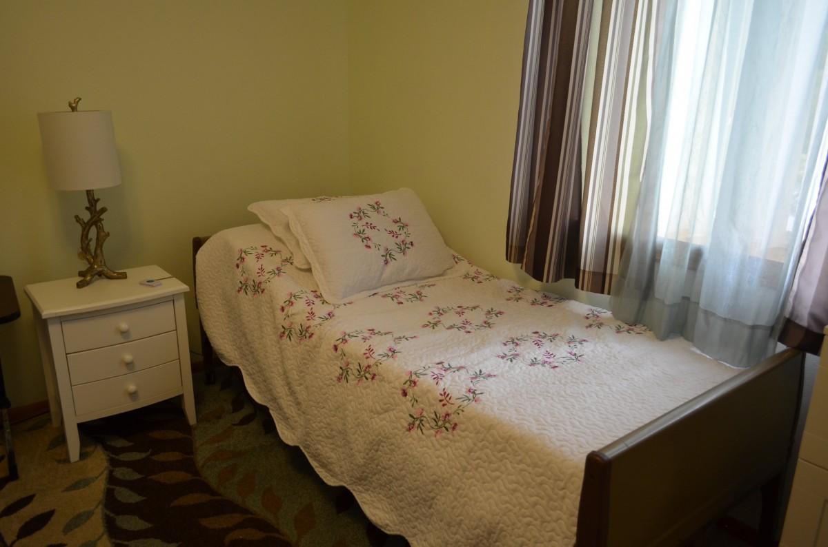 A cozy bedroom with a single bed and decorative bedding next to a small nightstand.