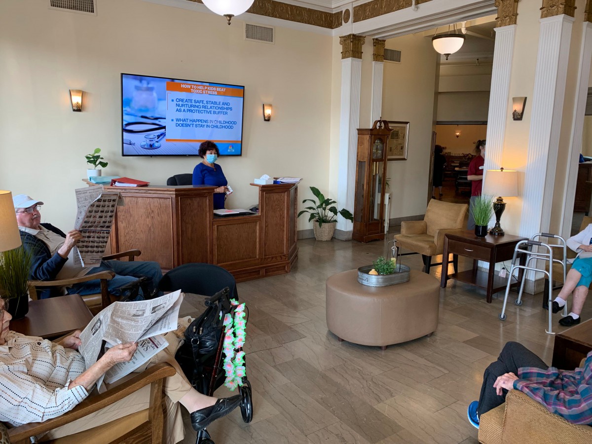 A modern lobby with people seated, a reception desk, and a television displaying information.