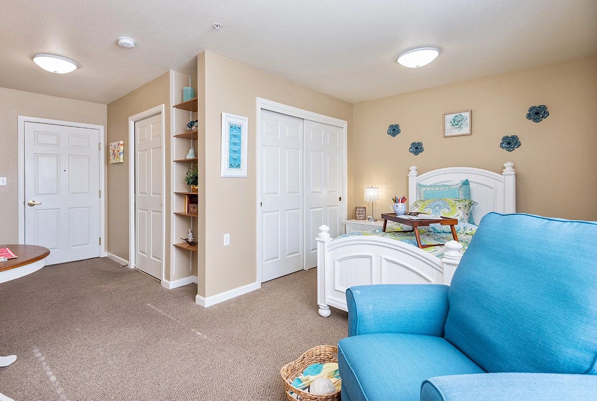 A cozy children's bedroom with a bed, blue armchair, and built-in shelves.