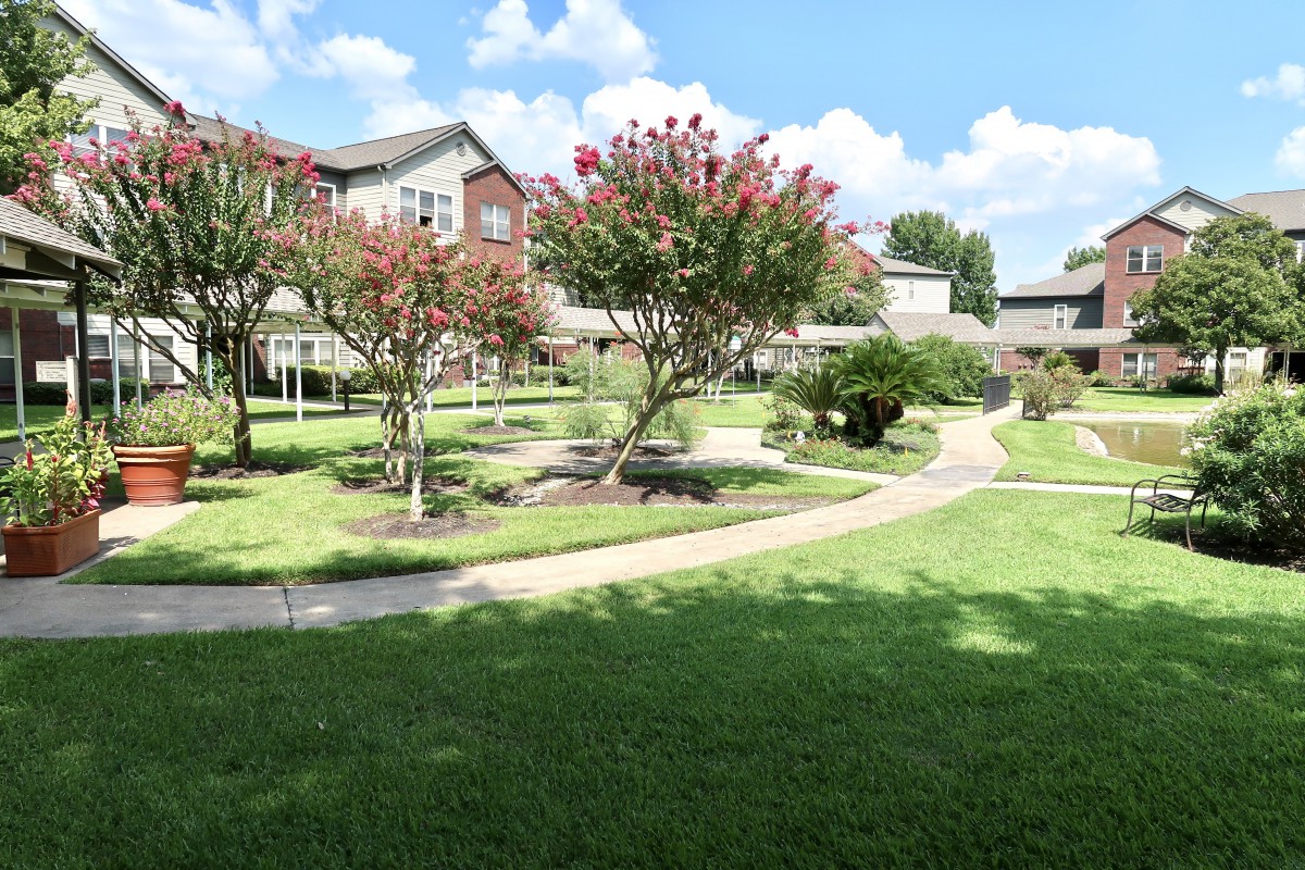 A beautifully landscaped garden with a winding pathway, trees, and a building in the background on a sunny day.