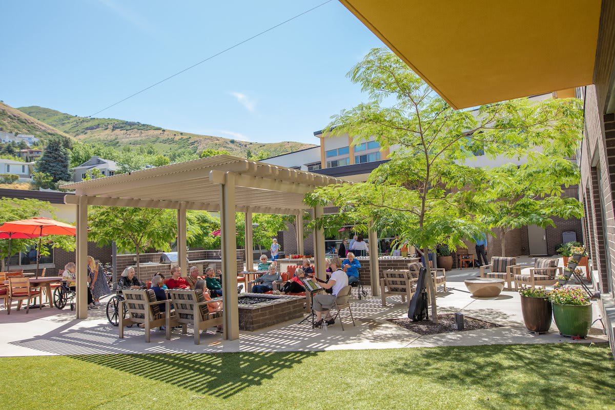 People enjoying a sunny day on an outdoor patio with shade structures and trees.