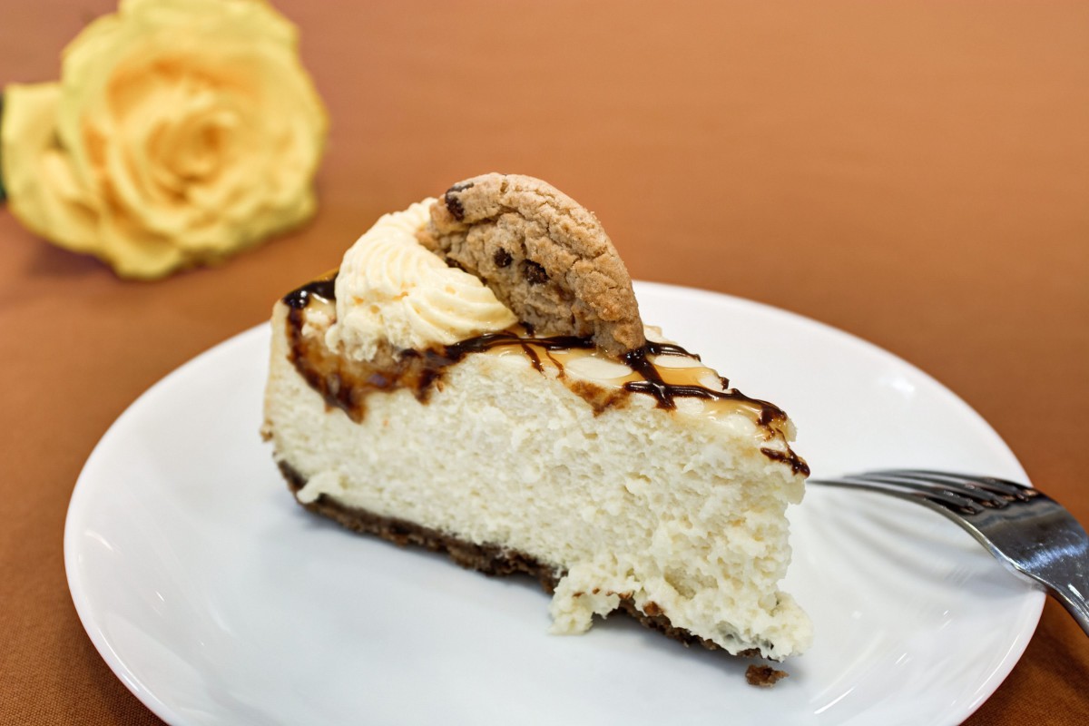 A slice of cheesecake topped with a cookie and drizzled with chocolate.