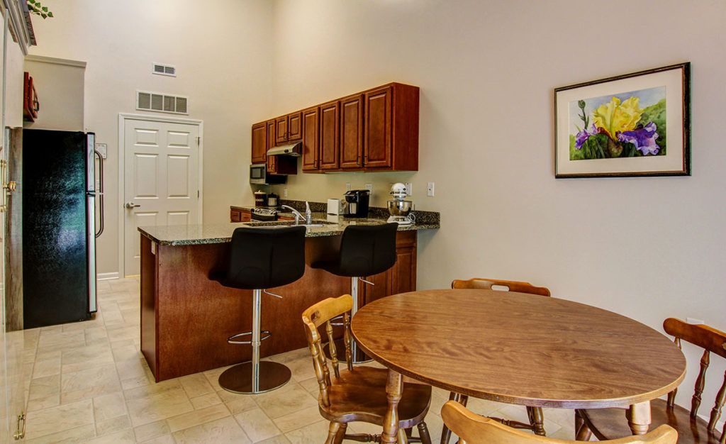 A modern kitchen with wooden cabinets, bar stools, and a round dining table.