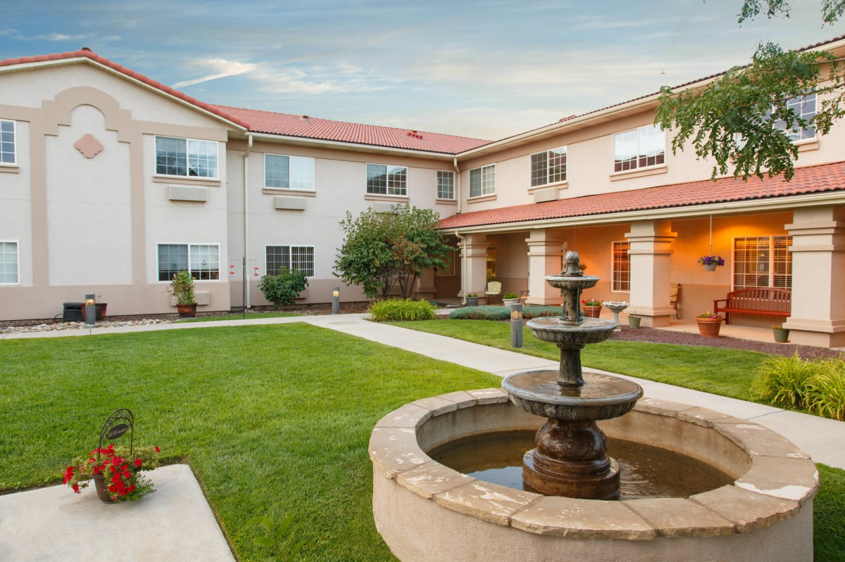 A well-maintained garden with a fountain in front of a two-story building.