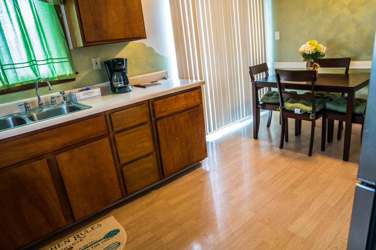 A cozy kitchen and dining area featuring wooden cabinets, a coffee maker, and a small round table with chairs near a sliding door.
