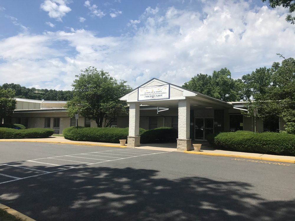 Entrance of a building surrounded by trees and a parking lot under a partly cloudy sky.