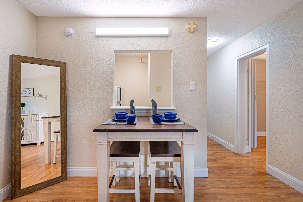 A cozy dining area features a table set for two with blue dishware, positioned next to a kitchen pass-through and adorned with wooden flooring.