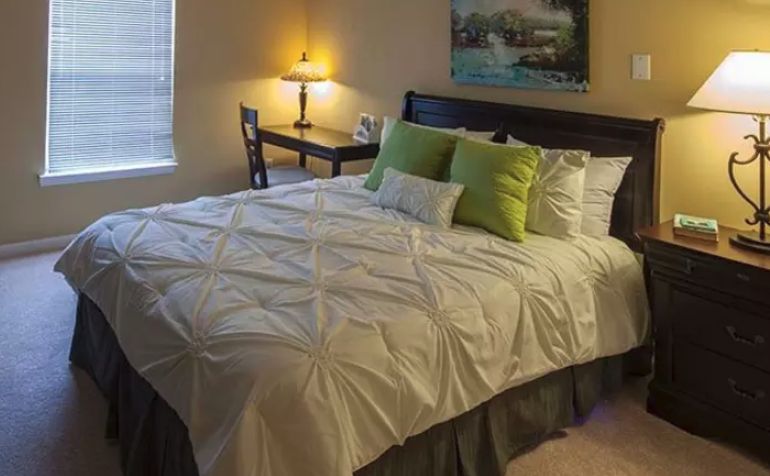 A cozy bedroom with a neatly made bed, desk, and lamp.