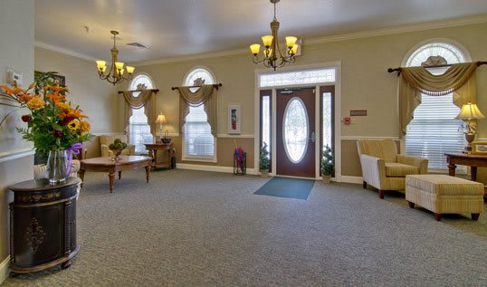 A spacious lobby with elegant chandeliers, carpeted flooring, and large windows draped with curtains.