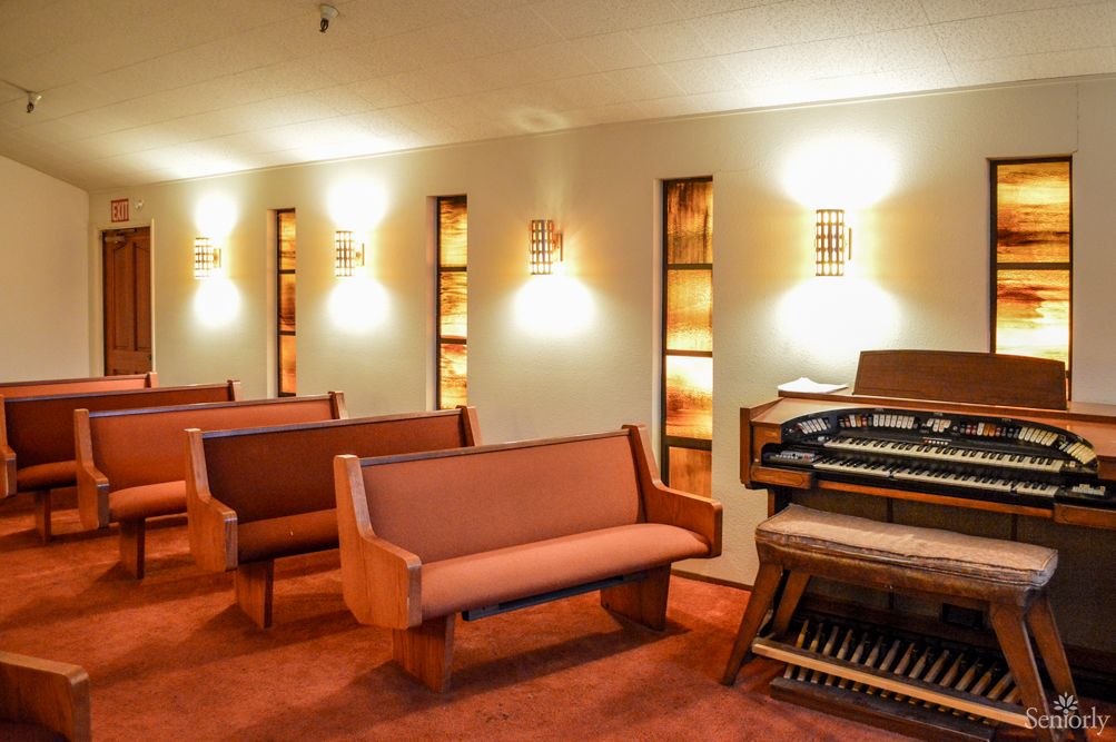 A well-lit church interior with wooden pews and a large organ against the wall.