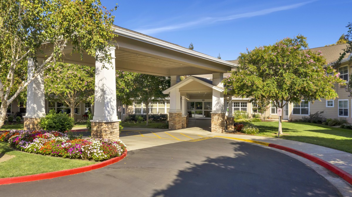 A building entrance with a covered driveway, surrounded by trees and well-maintained landscaping.