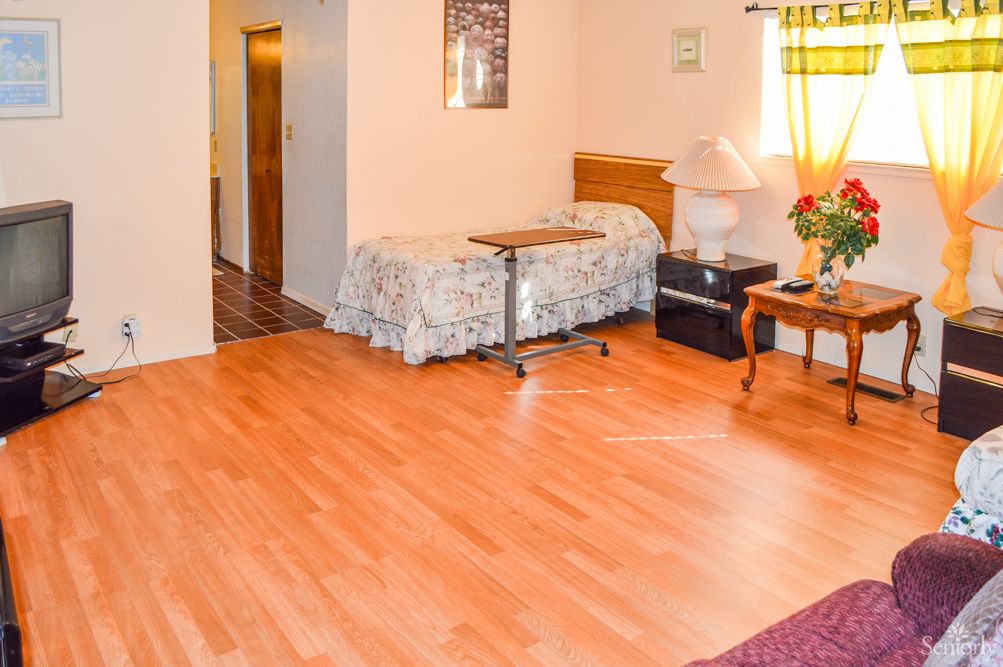 A cozy bedroom with hardwood flooring, featuring a bed, table, and lamp near a window.