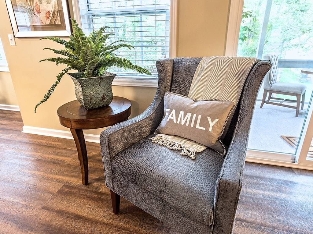 A cozy living room corner featuring a plush chair with 'Family' pillows, complemented by a potted plant on a wooden side table.