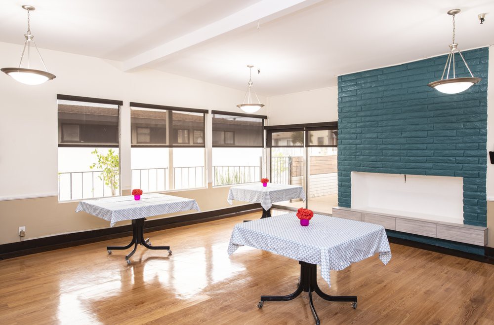 A modern dining area with tables set for guests, featuring white tablecloths and floral centerpieces.