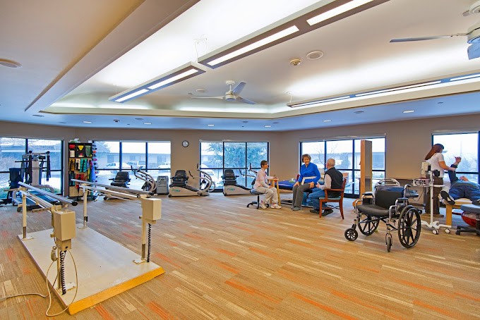 A spacious rehabilitation center with exercise equipment and people engaging in physical therapy.