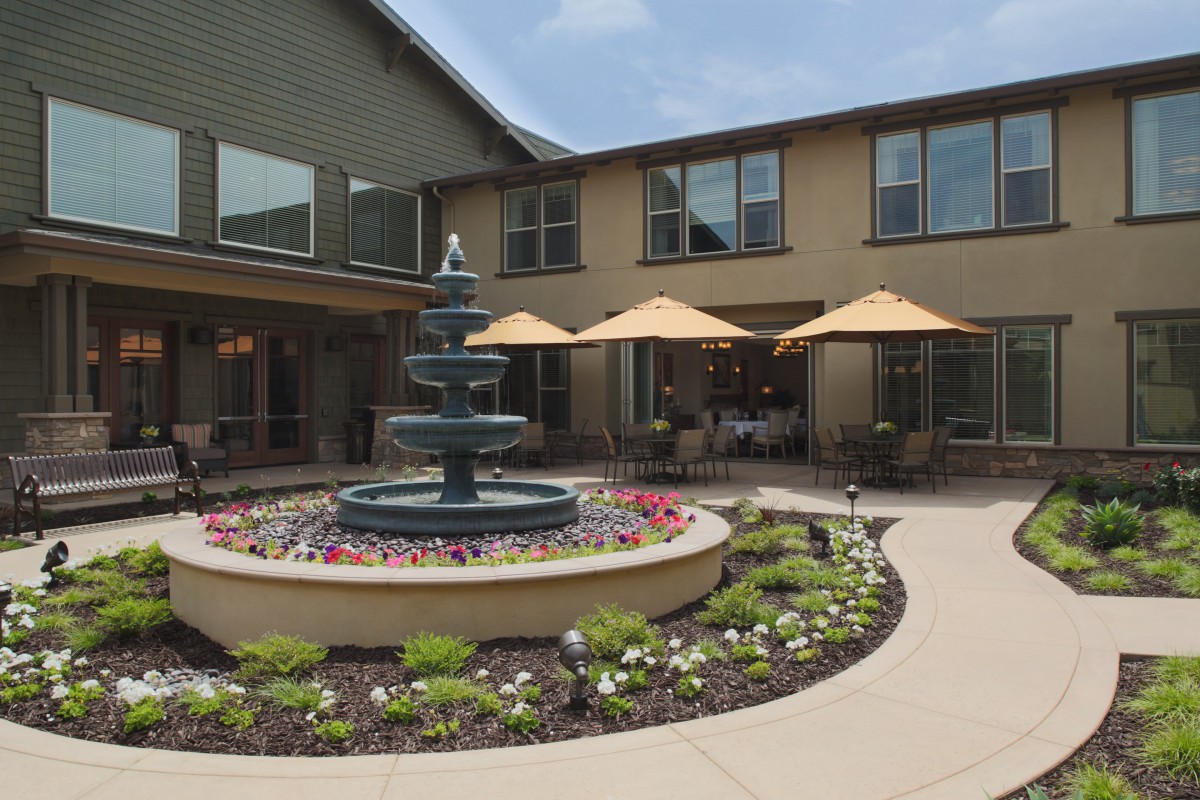 A peaceful courtyard featuring a central fountain, surrounded by lush landscaping and shaded seating areas.