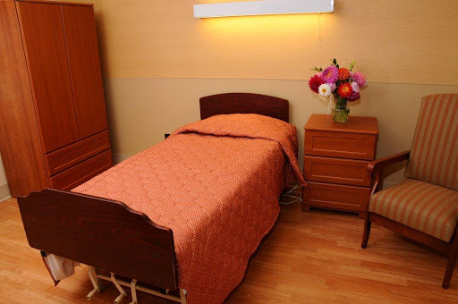 A cozy bedroom featuring a single bed with an orange blanket, a nightstand, and a vase of flowers.
