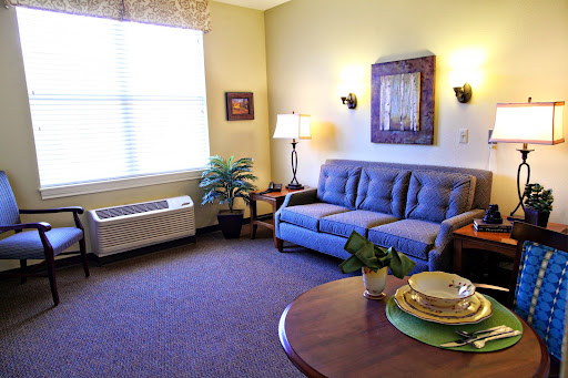A cozy living room featuring a blue sofa, a round table set with plates, and natural light streaming through the window.
