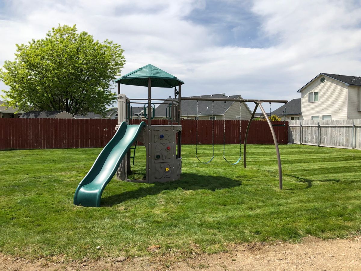 A backyard playground set featuring a slide and swings on a grassy lawn.