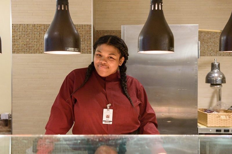 A person in a red uniform standing behind a counter in a kitchen area.