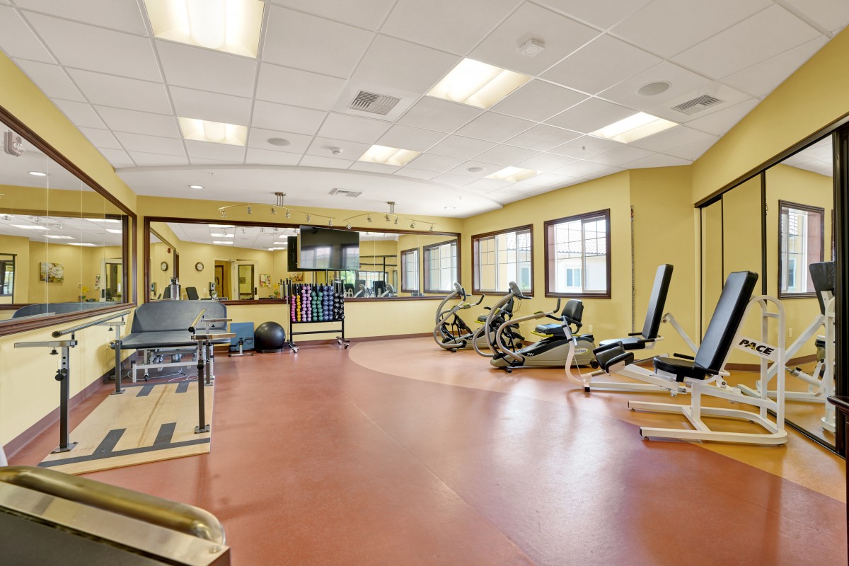 A well-lit gym with various exercise equipment and workout machines.